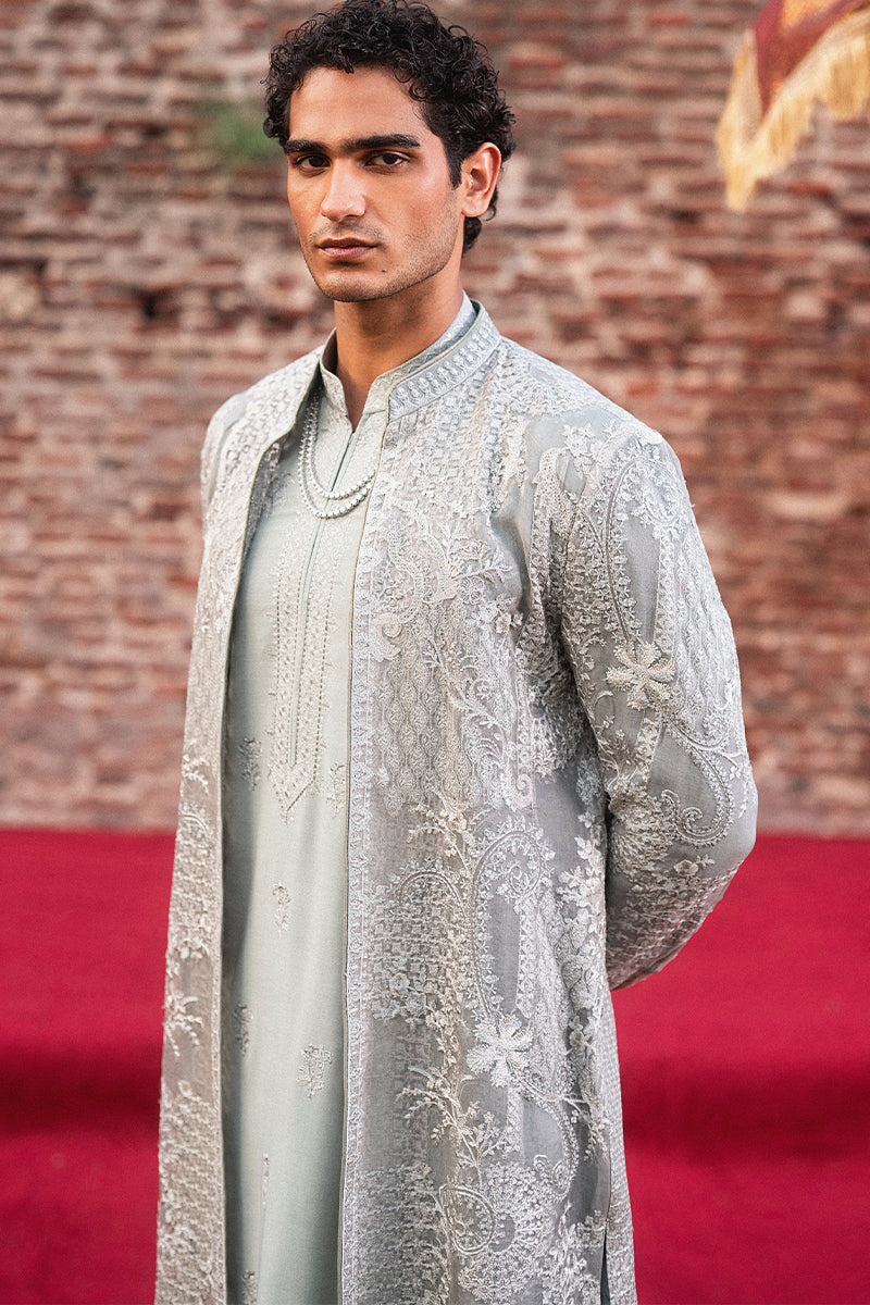 Man wearing a traditional embroidered sherwani against a brick wall background