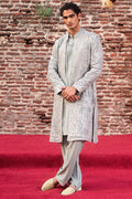 Man wearing a traditional outfit with a textured fabric against a brick wall.